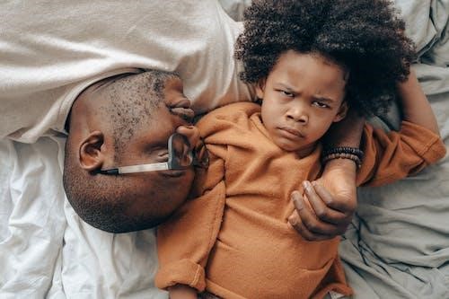 Child angry expression adult hugging child on bed